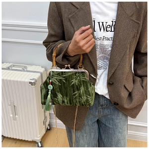 Detail of green velvet bag with bamboo handle and elegant tassels shown on a model