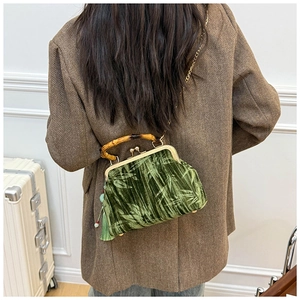 Detail of a dark green velvet bag with bamboo handle and elegant leaf pattern embroidery