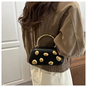 Details einer schwarzen Hartschalen-Abendtasche mit goldenen Kieselsteinen und Perlengriff