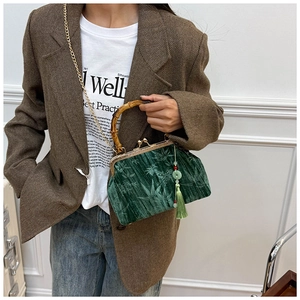 Macro detail of dark green velvet bag with bamboo handle and golden chain strap