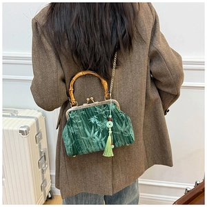 Detail of dark green velvet bag with bamboo handle and elegant green tassel on a model