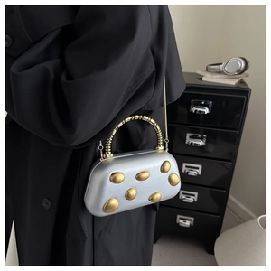 Silberne Kiesel-Abendtasche mit goldenen Punkten und Spiralgriff auf schwarzem Mantel
