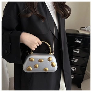 Details der silbernen matten Clutch mit goldenen Akzenten und Perlengriff auf schwarzem Schrank