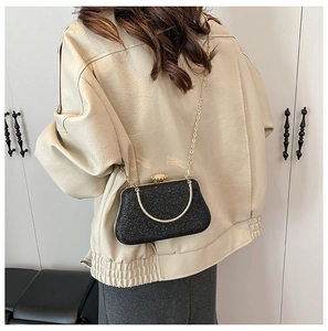 Detail of black sequin evening bag with gold chain strap and metal handle on beige jacket