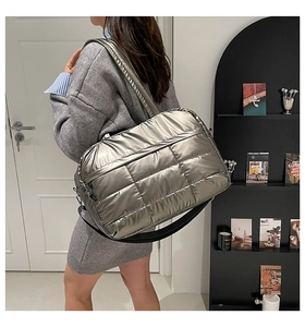 Detalle de un bolso tote acolchado plateado metalizado con correa ancha en una modelo