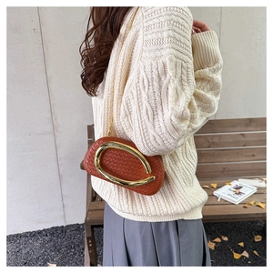 Brown woven clutch bag with large gold metal handle shown on a model in a casual style