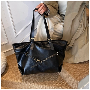 Detail of a large black vintage tote bag with gold hardware held by a model in a trench coat