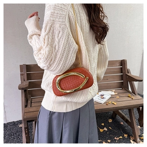 Detail of orange woven crossbody bag with gold ring handle worn over a beige sweater