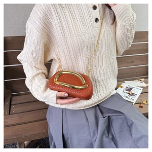 Detail of brick red woven clutch featuring a large gold metal handle and chain strap