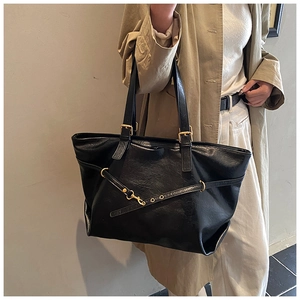 Detail of black leather tote bag featuring gold buckle hardware and natural grain texture
