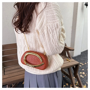 Brown woven clutch bag with gold U-shaped frame and chain strap shown on model outdoors