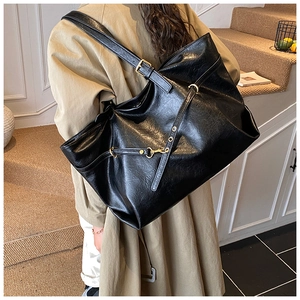 Detail of vintage black leather tote bag with gold metal buckles on a trench coat