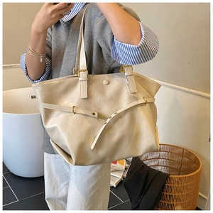 Detail of beige wrinkled leather tote bag with gold hardware worn on model shoulder