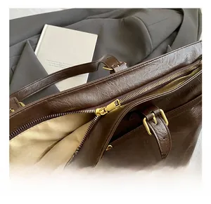 Detail of dark brown leather tote bag with gold metal zipper and polished hardware