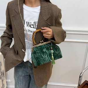 Dark green velvet bag with bamboo handle and leaf texture shown on a female model