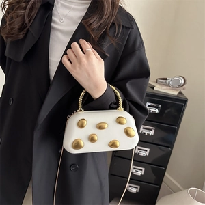 Weiße Abendtasche im Kiesel-Design mit Goldgriff und Kette auf schwarzem Mantel