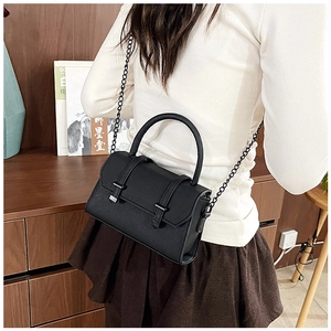 Chic black crossbody bag with metal chain strap worn over the shoulder in a cozy setting