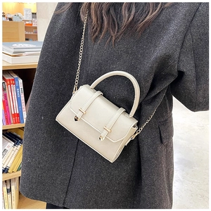 Chic beige crossbody bag with gold chain strap shown being worn in a cozy library setting