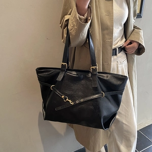 Glossy black faux leather tote bag with gold metal buckle shown on a model