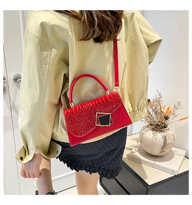 Close-up of vibrant red crocodile pattern leather bag with gold buckle on beige coat
