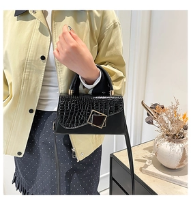 Detail of a black faux crocodile leather crossbody bag featuring a golden square lock