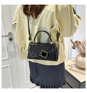 Detail of black faux leather handbag with crocodile pattern flap and gold square buckle