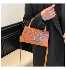 Detail showing orange crocodile texture leather and geometric silver buckle on handbag
