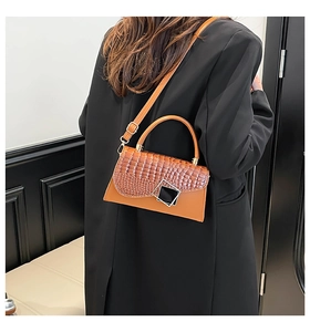 Detail der braunen Handtasche mit Krokodilmuster und quadratischer Metallschnalle am Modell
