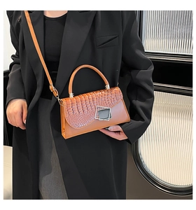 Detail of a brown crocodile texture crossbody bag with geometric metal buckle on black suit