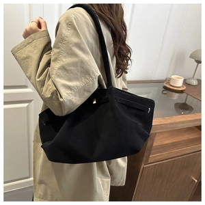 Side view of large black matte suede tote bag worn with a khaki trench coat