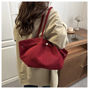 Dettaglio di una borsa tote in pelle scamosciata bordeaux con cinturini decorativi e fibbia