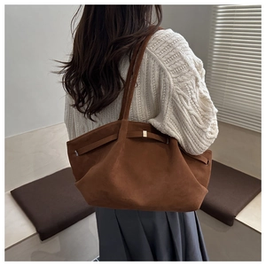 Detail of a deep brown suede tote bag with metal buckle on a white cable knit sweater
