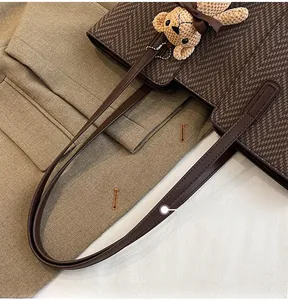 Detail of brown herringbone tote bag with leather handles and a plush bear pendant