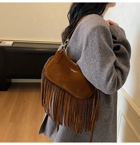Close-up of brown suede dumpling bag featuring decorative tassels and gold metal zippers