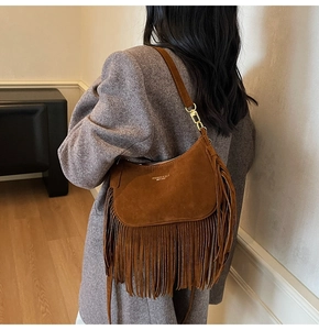 Detail of brown suede hobo bag with long fringes and fashion engraving worn with a grey coat