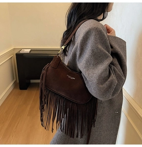 Detailed shot of dark brown suede shoulder bag with long fringe and gold metal buckle