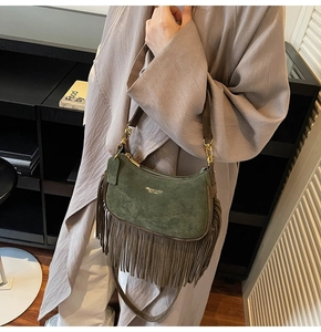 Detail of dark green suede dumpling bag with long fringe tassels and golden logo