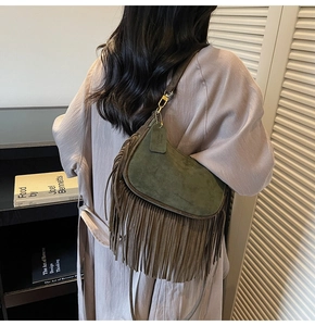 Detail of dark green suede saddle bag with long fringe tassels and vintage metal buckle