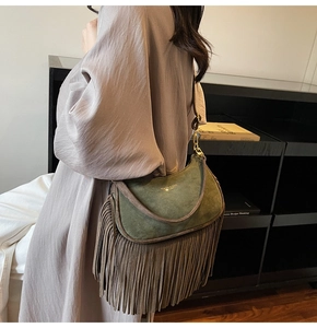 Detail of dark green suede crossbody bag featuring long brown tassels and gold logo