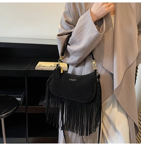 Detail of black suede tassel bag with golden metal chain on a grey coat background