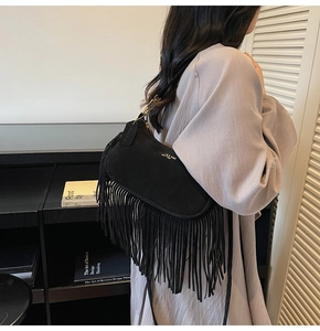 Detail of black suede shoulder bag featuring long fringe tassels and brand metal charm