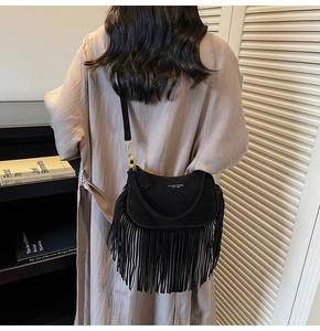 Close-up of black suede tassel crossbody bag with metallic logo and golden hardware