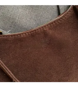 Macro detail of dark brown suede texture with golden branding on a crossbody bag