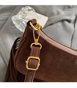 Close-up of brown suede bag featuring gold-tone hardware, zipper detail and side fringe