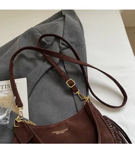 Detailed view of dark brown suede shoulder bag with tassel and gold logo lettering