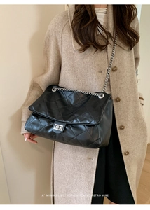 Detail of black quilted leather tote bag with silver chain strap and metal turn-lock