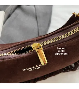 Close-up of smooth gold metal zipper and logo on brown suede underarm handbag