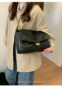 Classic black quilted tote bag with gold chain strap shown on a khaki trench coat