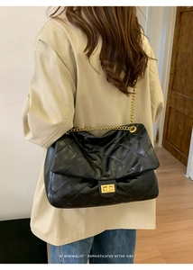 Detail of classic quilted texture and gold metal chain strap on large black tote bag