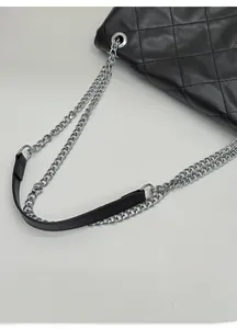 Detail of black quilted leather shoulder bag with silver chain strap and metal buckles